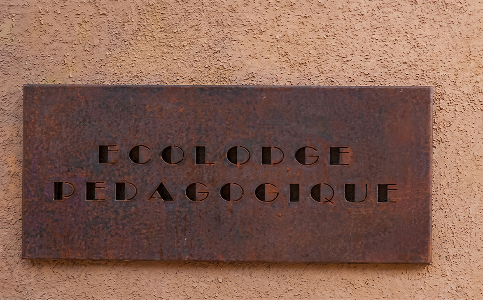 Enseigne Ecolodge pédagogique découpée dans une plaque en Acier Corten fixée sur un mur extérieur