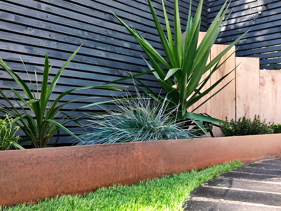 Long bac jardinière en acier Corten avec plantes décoratives dans un jardin contemporain