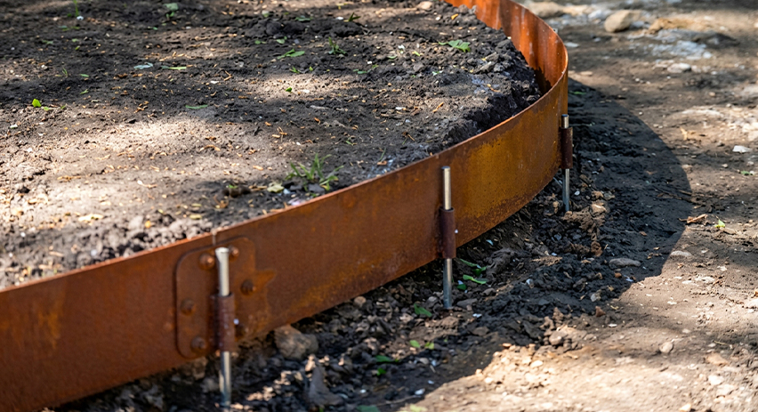 Fabrication Corten sur mesure d’une bordure de jardin courbe fixée au sol par des piquets métalliques